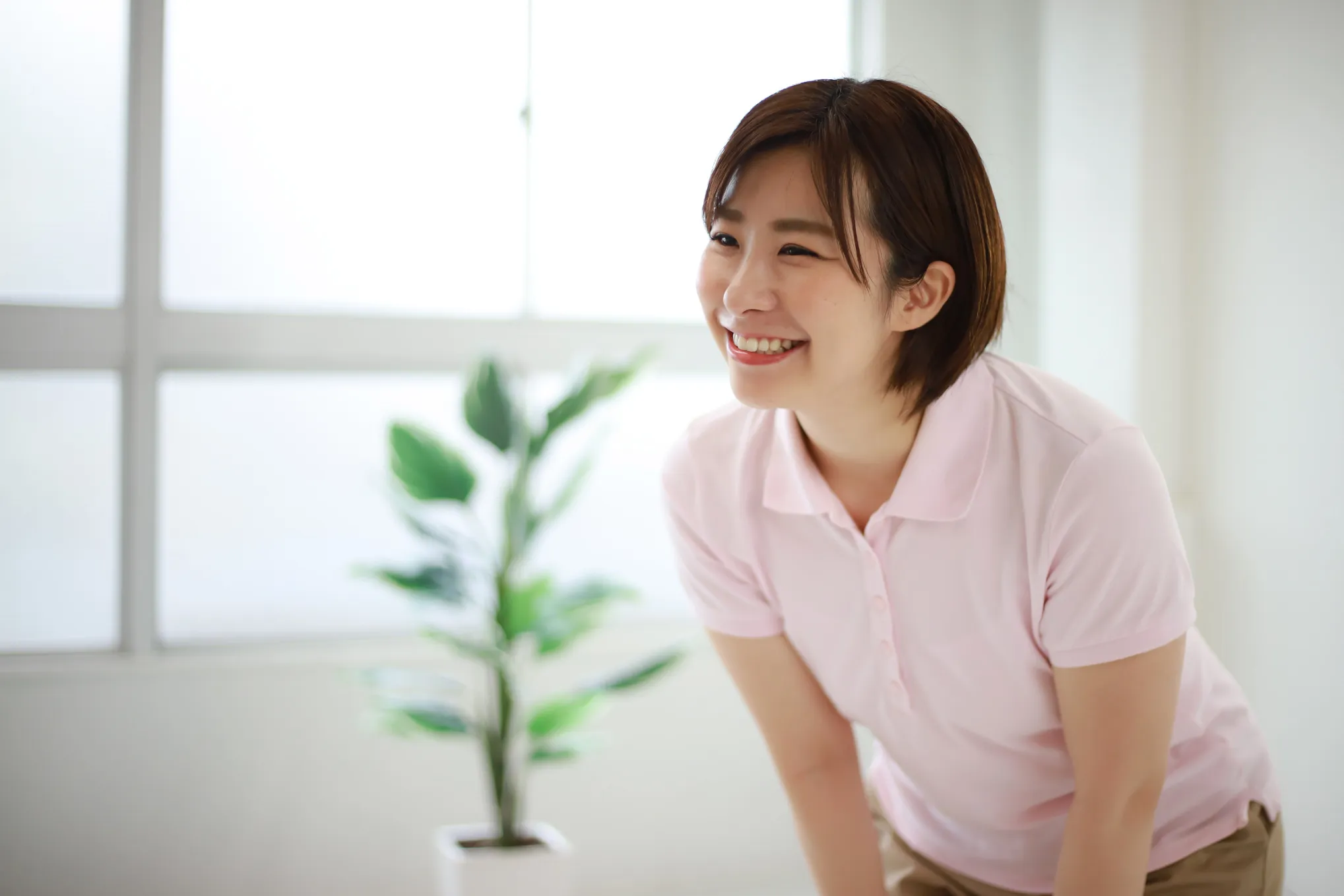 室内で明るく微笑む、ピンクのポロシャツ姿の女性介護スタッフ